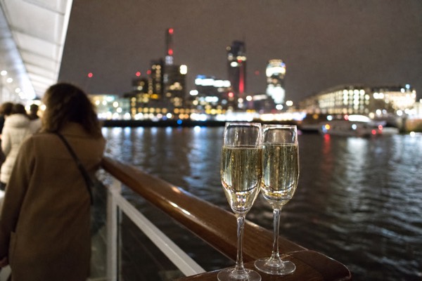 Glasses of sparkling wine on the deck of an evening Thames cruise with the city lights behind