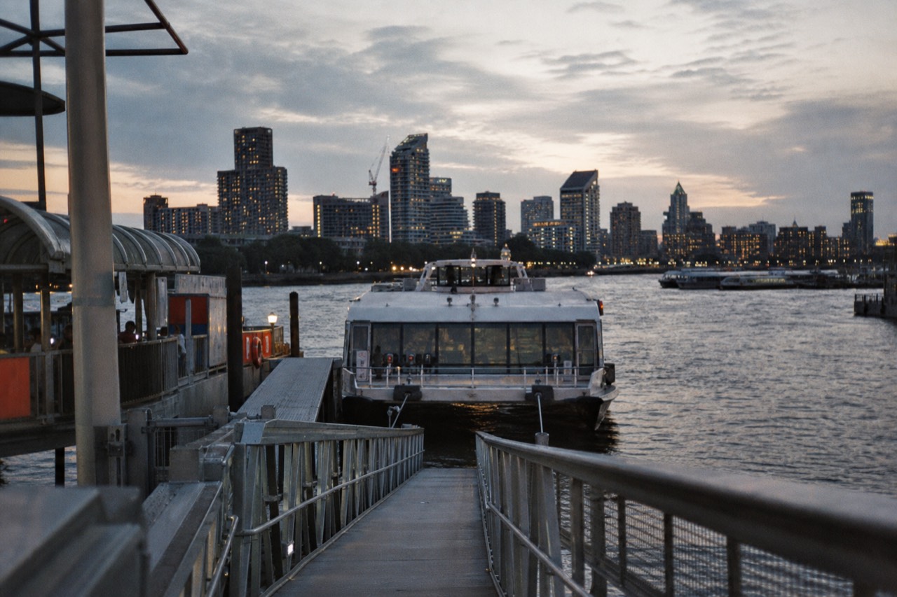 A sightseeing boat approaching a floating pier in late afternoon light, gangway lowered and the river wide behind it