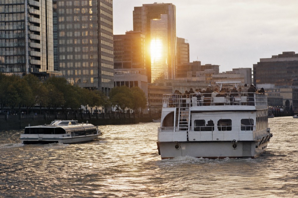 Two very different passenger boats sharing the same stretch of river, one low and fast, one tall with an open upper deck