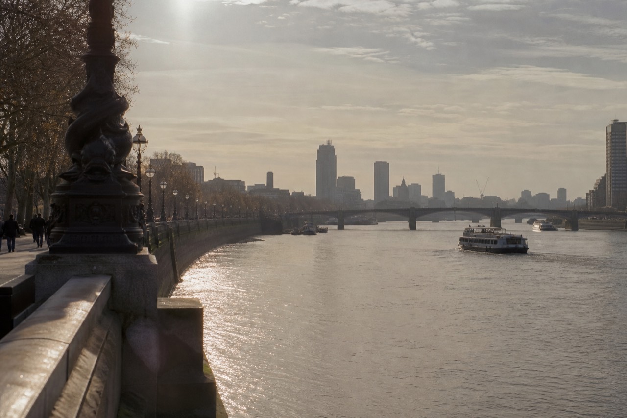 The Thames curving through central London in low winter sun, bridges stepping away into haze and the water running silver against dark embankment walls