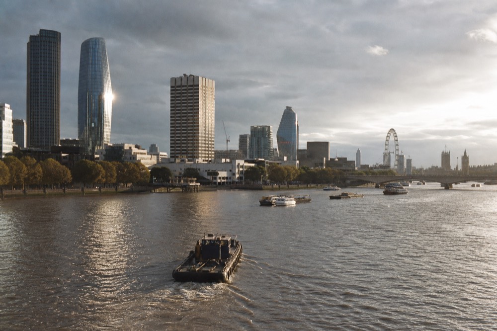 Low afternoon sun raking across City towers and a river bank seen from mid-stream, long shadows on the water