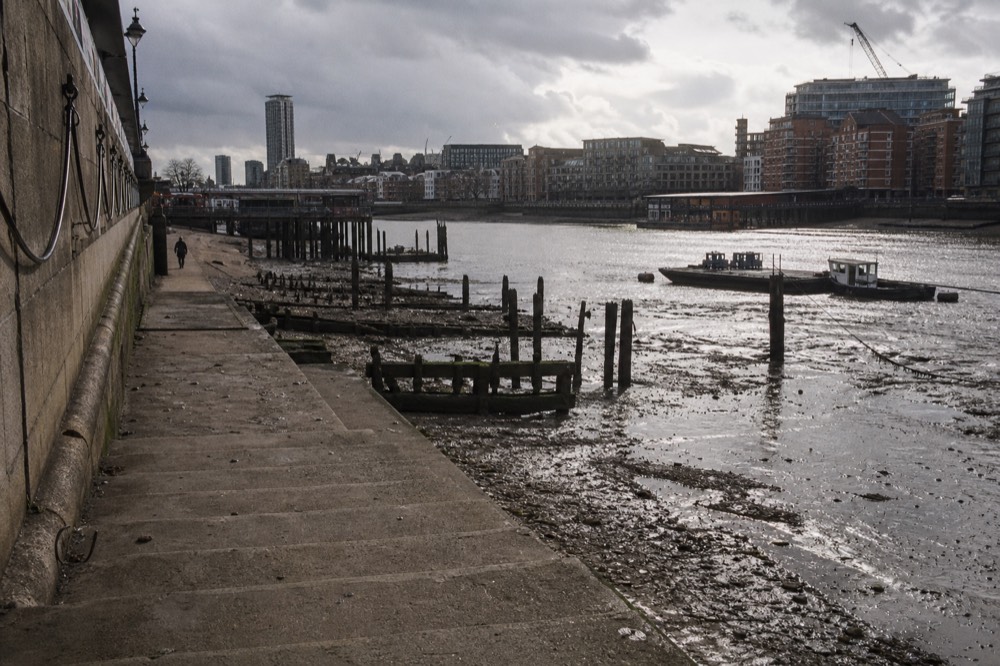 Worn stone river stairs running down to a wide expanse of exposed foreshore at low tide, wooden barge beds and rotting piles emerging from the mud