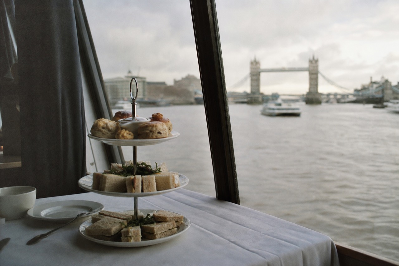 Tiered afternoon tea stand beside a window on a daytime Thames cruise