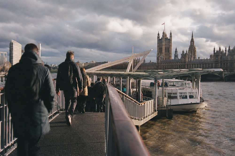 Passengers boarding a river boat at Westminster Pier in early morning light, Houses of Parliament rising above the pontoon