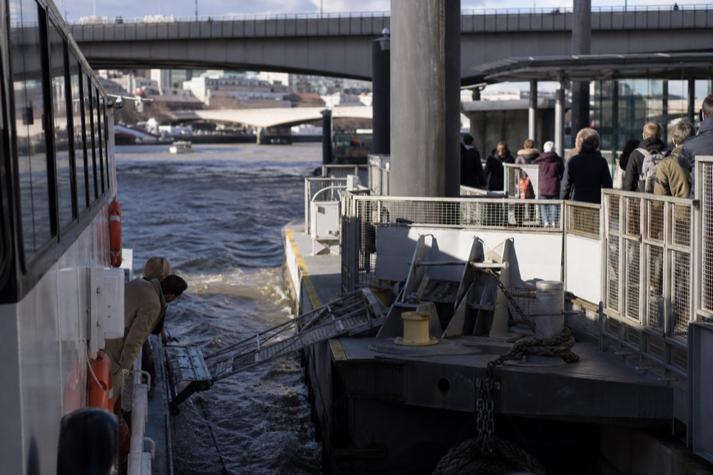 A river boat drawing alongside a floating pier pontoon with a gangway lowered, passengers waiting on the deck above