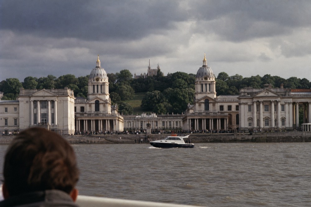 The classical riverfront at Greenwich seen from mid-river, twin domes and colonnades with the wooded hill and observatory rising behind