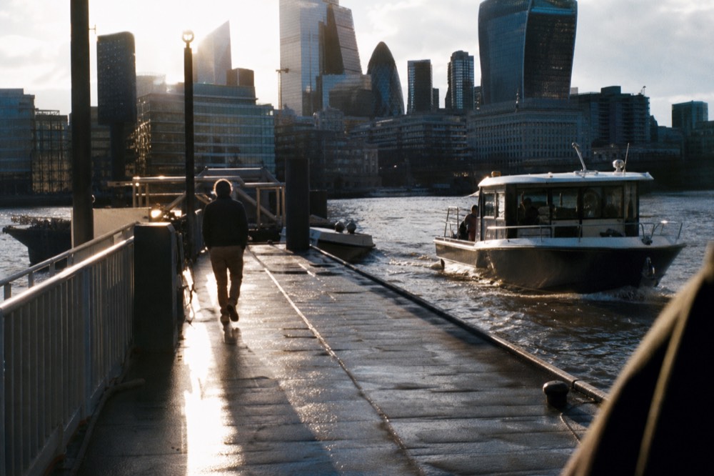 Late afternoon light on a river pontoon with long shadows across wet decking and a boat easing in alongside