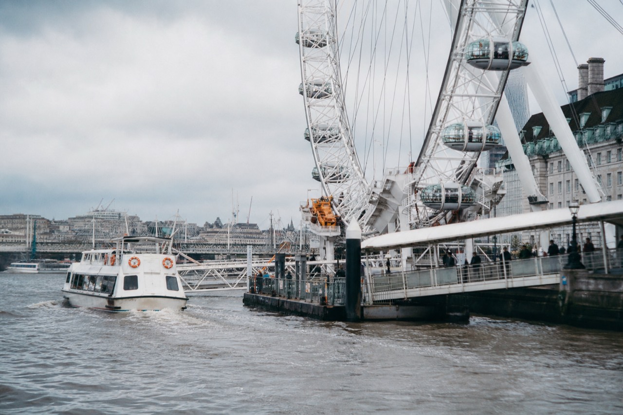 Cruise boat passing below the London Eye with Big Ben across the river