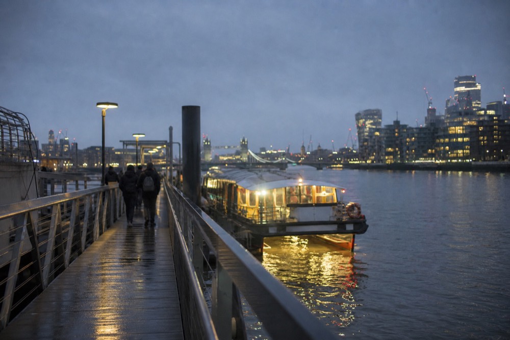 A floating pier on the river at blue hour with a lit passenger boat alongside and the water reflecting the bank lights