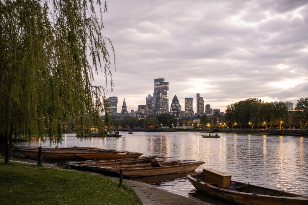 Wooden punts and small rowing boats tied along a green riverbank on a still summer afternoon, willows overhanging the water