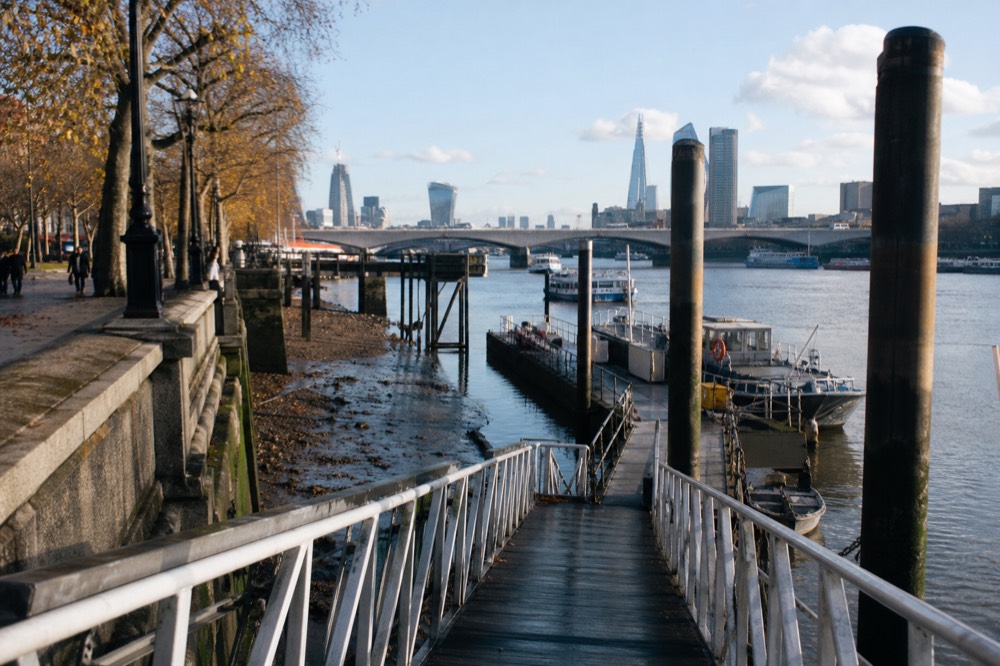 A steep pier gangway running down to a pontoon at low tide, wet timber and exposed foreshore below the embankment wall