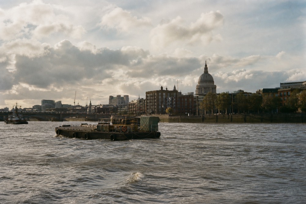 The dome of a large cathedral rising above riverside buildings on the north bank, seen from mid-river under bright cloud