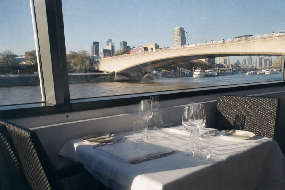 An empty laid table for four on a river boat with bright midday light through the window and a bridge passing outside