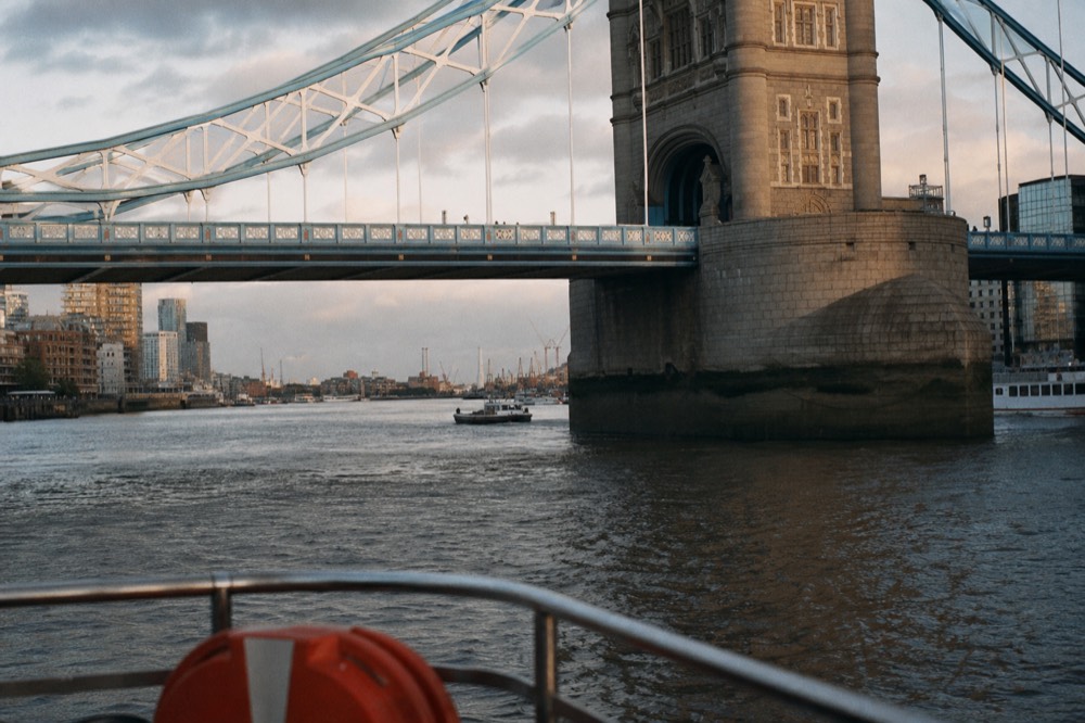 The river seen from a low boat deck just downstream of Tower Bridge, the channel widening east towards wharves under a bright sky