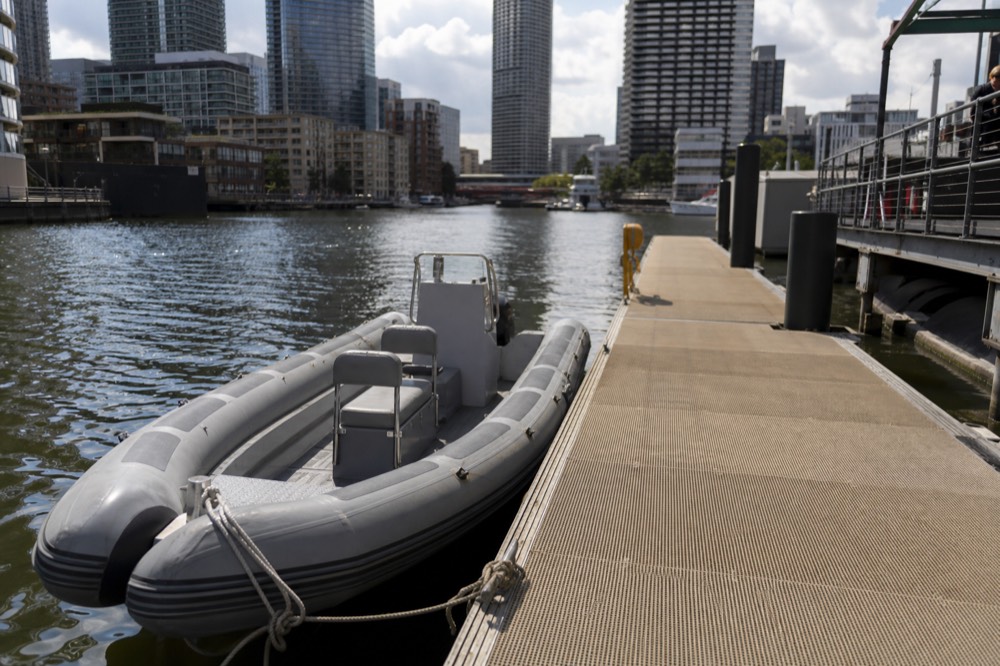 An empty rigid inflatable boat tied alongside a floating pontoon pier on a calm morning, grey tubes and bench seating visible, no markings