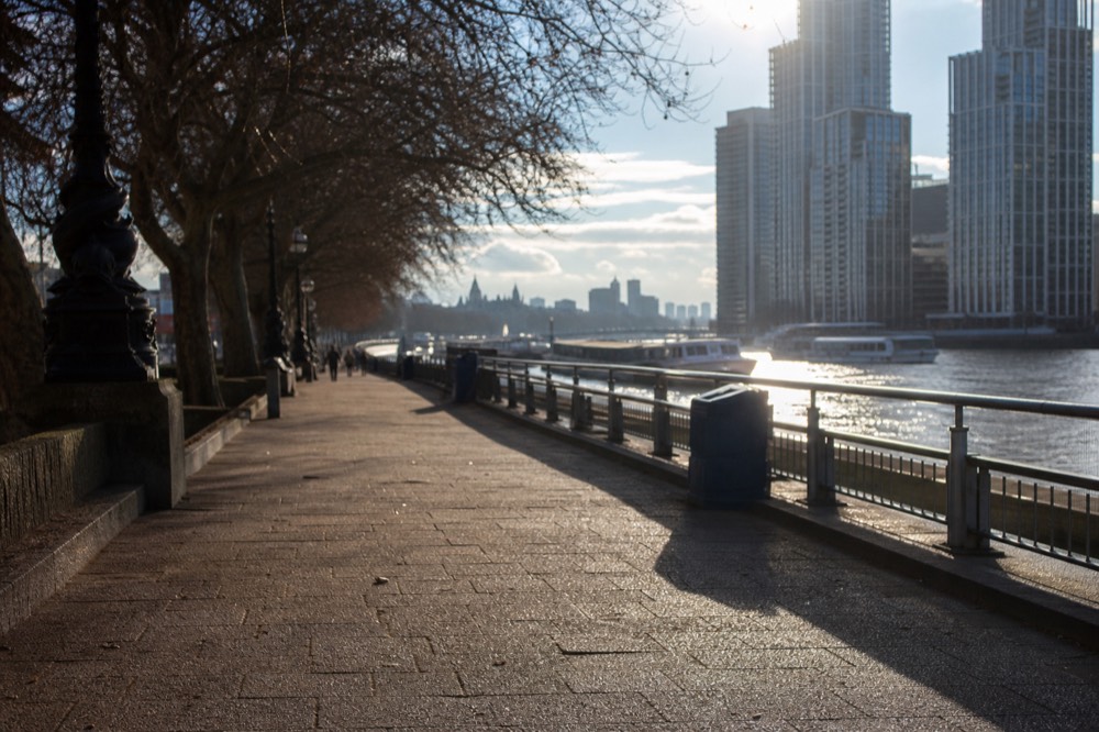 A near-empty river pier on a cold bright winter afternoon, low sun on the water and bare trees along the embankment