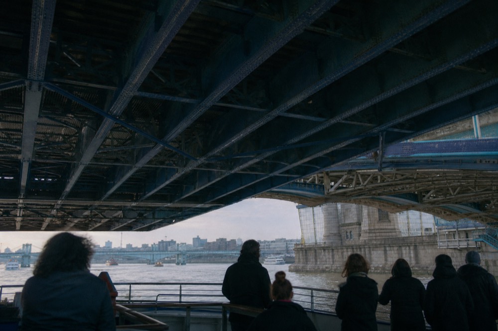 Looking up at the underside of a bascule bridge from a boat deck, blue ironwork and high walkways against pale sky