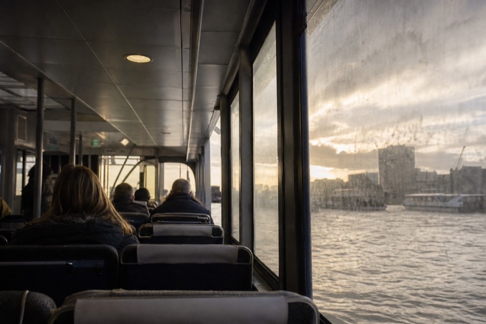 The interior saloon of a river commuter boat, rows of seats facing forward and grey river light through a salt-marked window