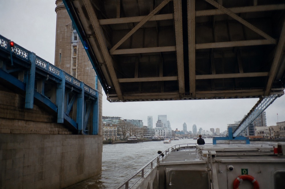 The underside of a raised bascule bridge with blue ironwork and high walkways, seen from the deck of a boat passing beneath